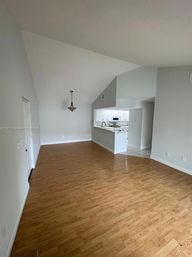 unfurnished living room with light wood finished floors, baseboards, a sink, and lofted ceiling