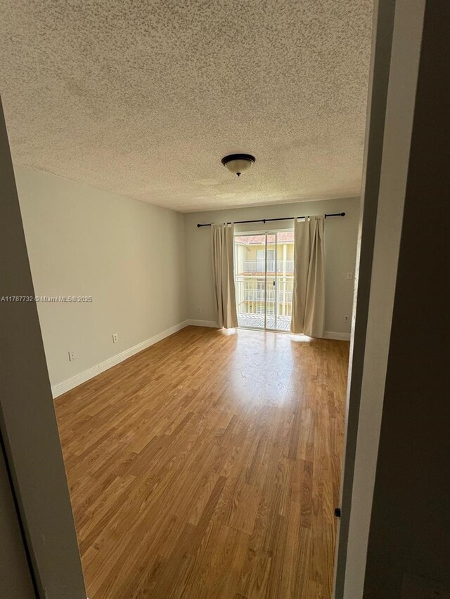 unfurnished room with wood finished floors, a textured ceiling, and baseboards
