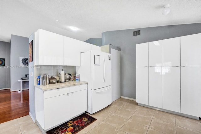 kitchen with freestanding refrigerator, light countertops, light tile patterned flooring, vaulted ceiling, and a textured ceiling