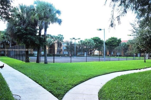 view of property's community featuring fence, a yard, and a tennis court
