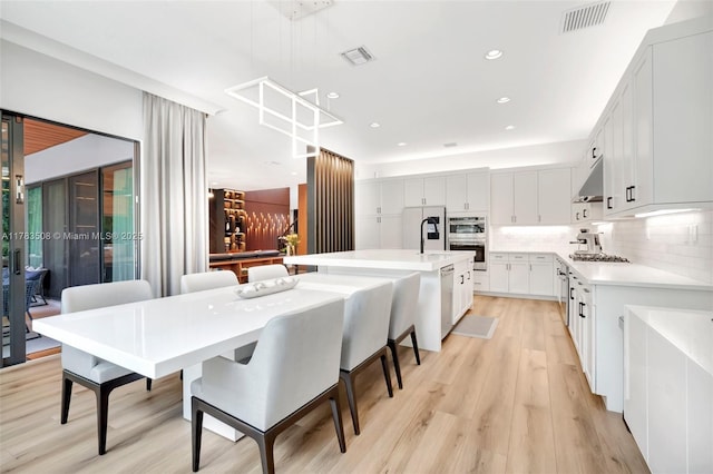8608 Torrey Isles Ter, Boca Raton, FL 33496 - kitchen with under cabinet range hood, light countertops, light wood-style flooring, backsplash, and a center island with sink