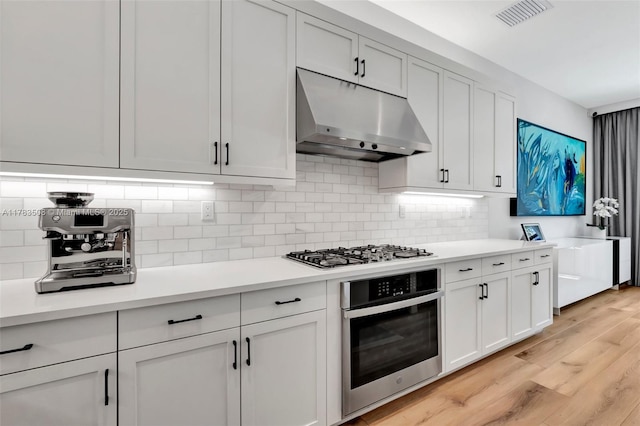 8608 Torrey Isles Ter, Boca Raton, FL 33496 - kitchen featuring stainless steel appliances, under cabinet range hood, light wood-style flooring, light countertops, and backsplash
