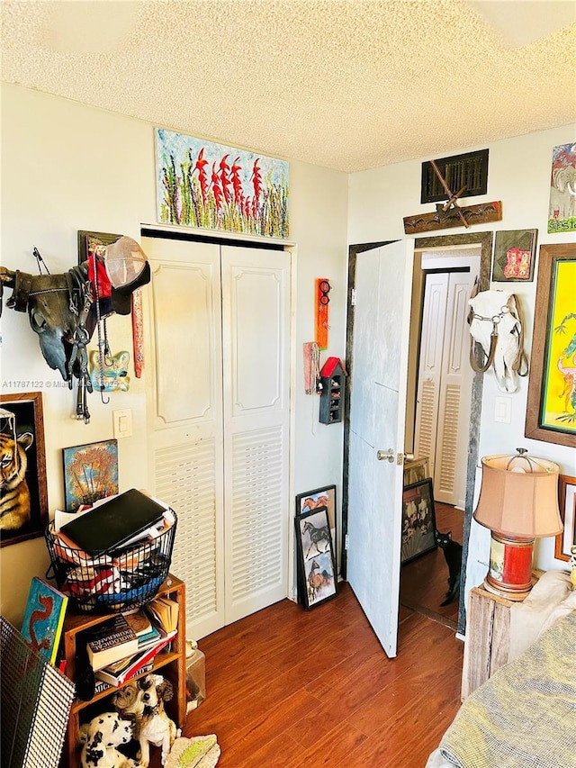 bedroom with a textured ceiling, wood finished floors, a closet, and visible vents