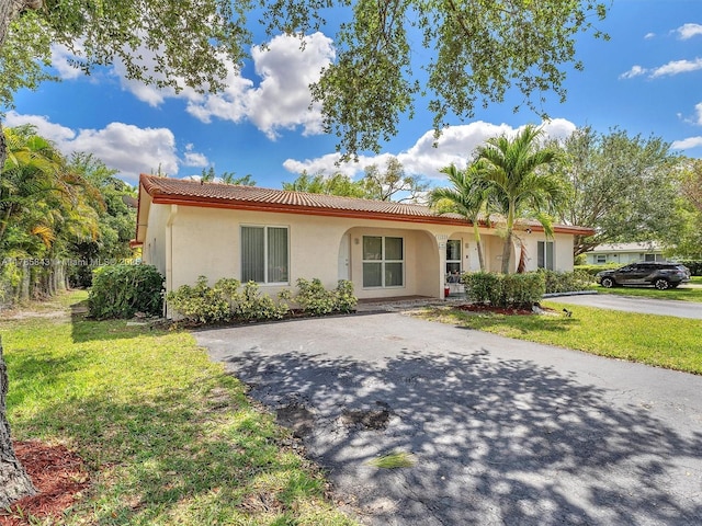 ranch-style home featuring stucco siding, a tile roof, driveway, and a front lawn