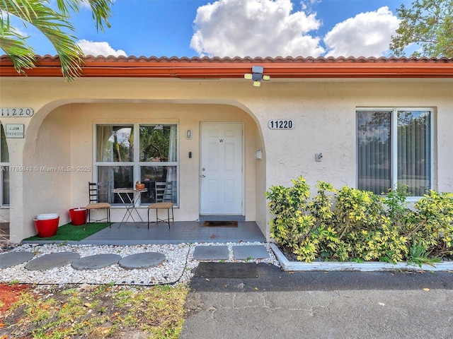 entrance to property featuring stucco siding, a tiled roof, and covered porch