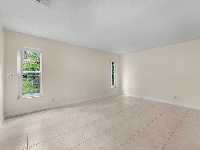 spare room with light tile patterned flooring, a textured ceiling, a wealth of natural light, and baseboards