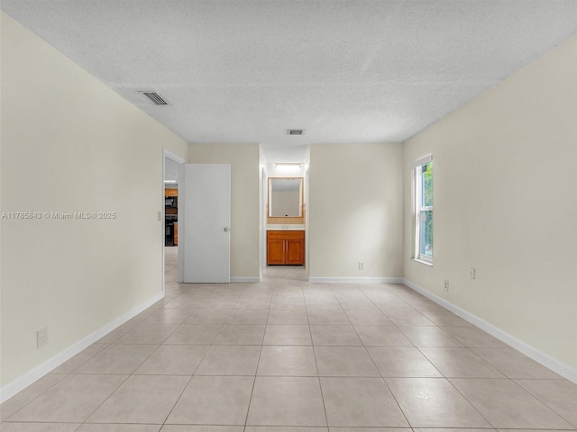 empty room with baseboards, visible vents, a textured ceiling, and light tile patterned flooring