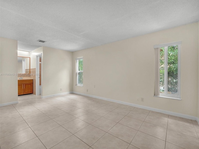 spare room featuring a healthy amount of sunlight, a textured ceiling, visible vents, and light tile patterned floors