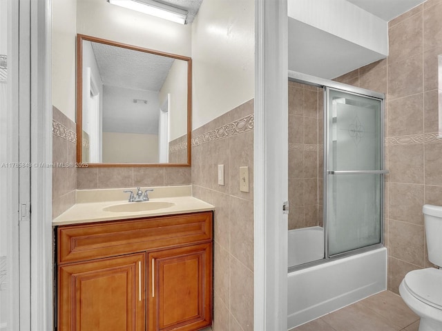 full bath featuring vanity, tile walls, bath / shower combo with glass door, toilet, and tile patterned flooring