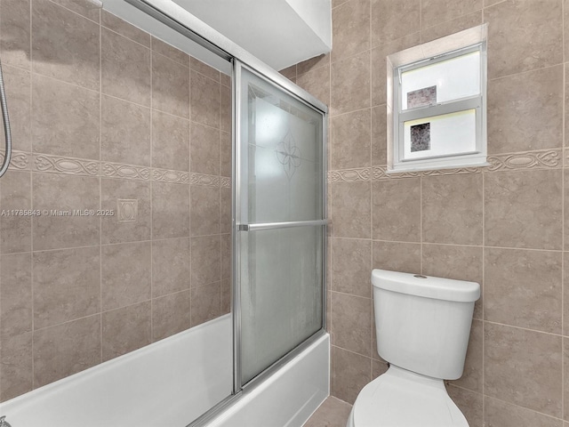 full bath with tile walls, combined bath / shower with glass door, and toilet
