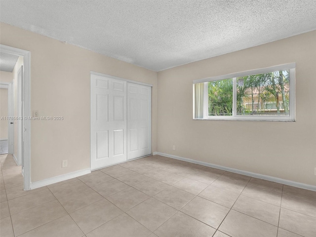 unfurnished bedroom featuring light tile patterned flooring, a closet, a textured ceiling, and baseboards