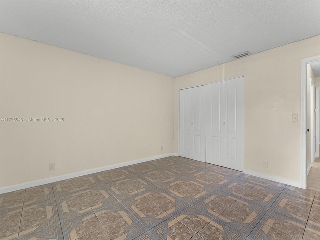 unfurnished bedroom featuring a textured ceiling, a closet, visible vents, and baseboards