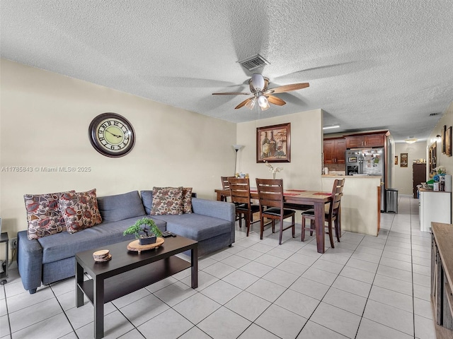 living area featuring light tile patterned floors, visible vents, a textured ceiling, and ceiling fan