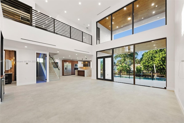 unfurnished living room with baseboards, recessed lighting, finished concrete floors, a high ceiling, and stairs