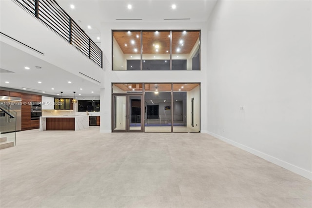 unfurnished living room with baseboards, a high ceiling, recessed lighting, and finished concrete flooring