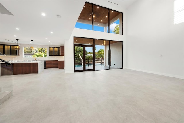 unfurnished living room with baseboards, a high ceiling, a wealth of natural light, and recessed lighting