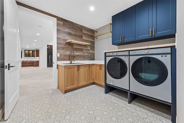 clothes washing area featuring washing machine and clothes dryer, a sink, wooden walls, cabinet space, and recessed lighting