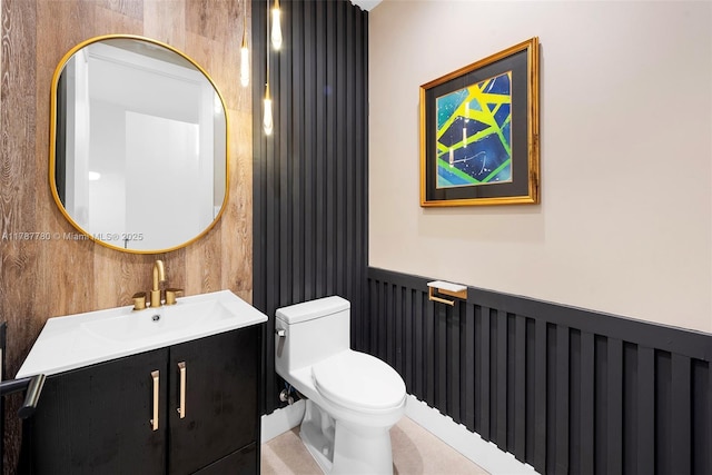 half bath with vanity, toilet, and a wainscoted wall