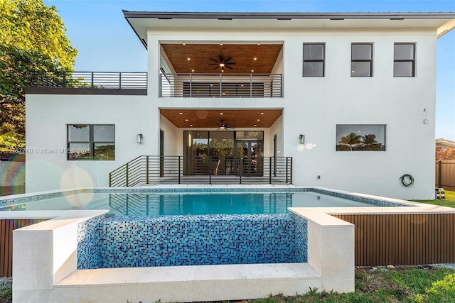 rear view of property with stucco siding, ceiling fan, an outdoor pool, and a balcony
