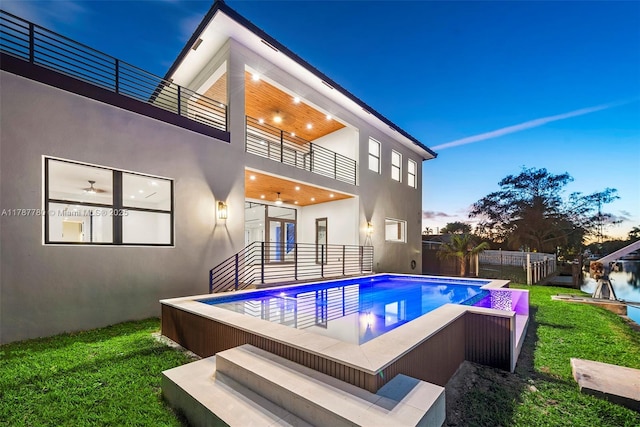 back of property with a balcony, a lawn, a fenced backyard, a fenced in pool, and stucco siding
