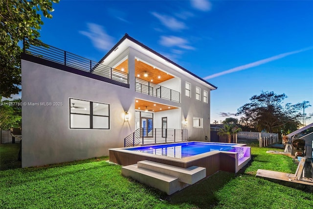 rear view of property featuring a fenced in pool, a fenced backyard, a lawn, a balcony, and stucco siding