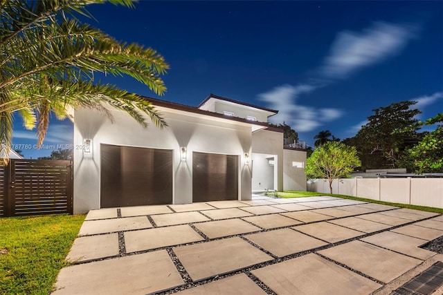 garage at night featuring fence and driveway