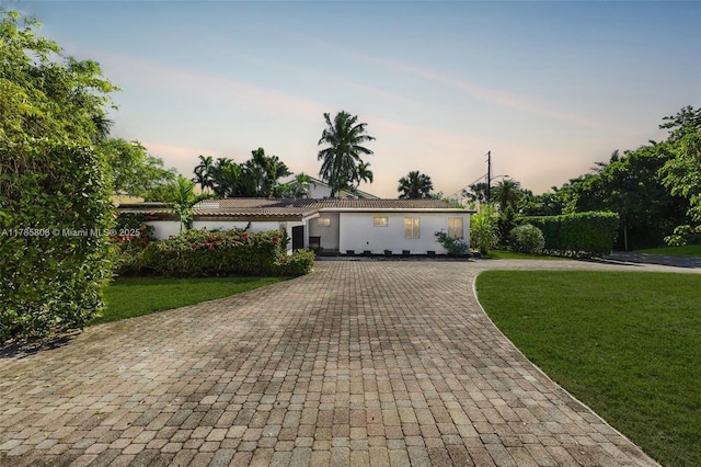 ranch-style home featuring stucco siding, a yard, a tiled roof, and decorative driveway