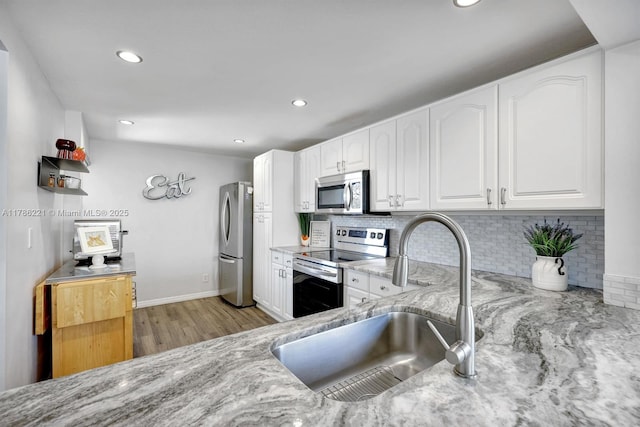 kitchen with light wood finished floors, stainless steel appliances, a sink, decorative backsplash, and light stone counters