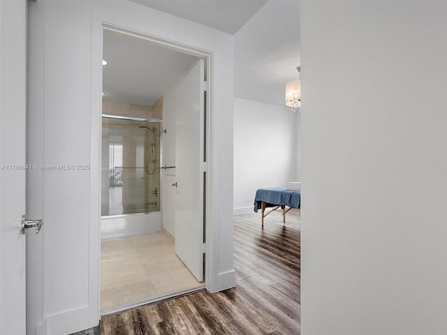 hallway featuring baseboards, a chandelier, and wood finished floors