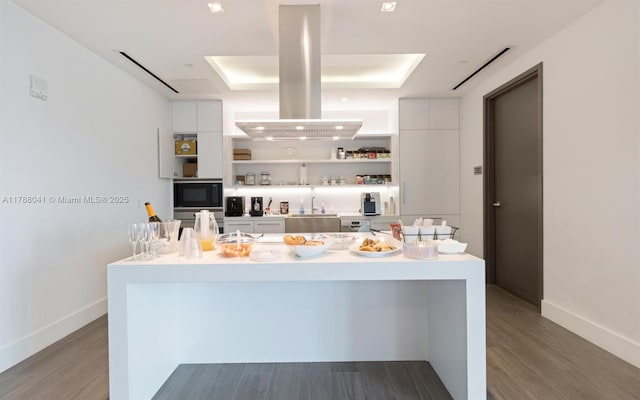 kitchen featuring open shelves, wood finished floors, island range hood, black microwave, and white cabinetry