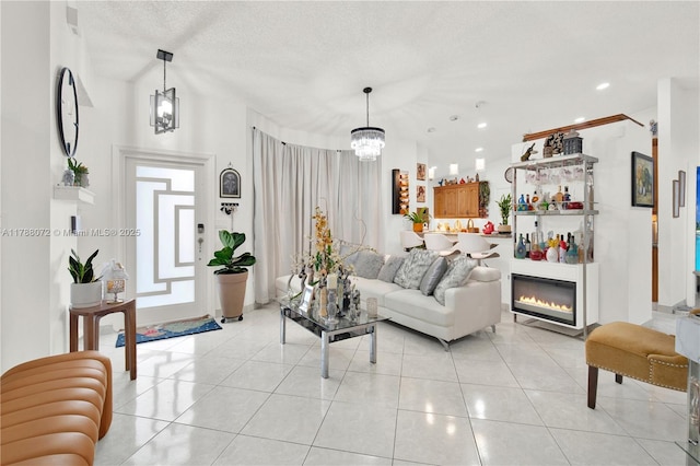 living room featuring recessed lighting, light tile patterned floors, a glass covered fireplace, a textured ceiling, and a notable chandelier
