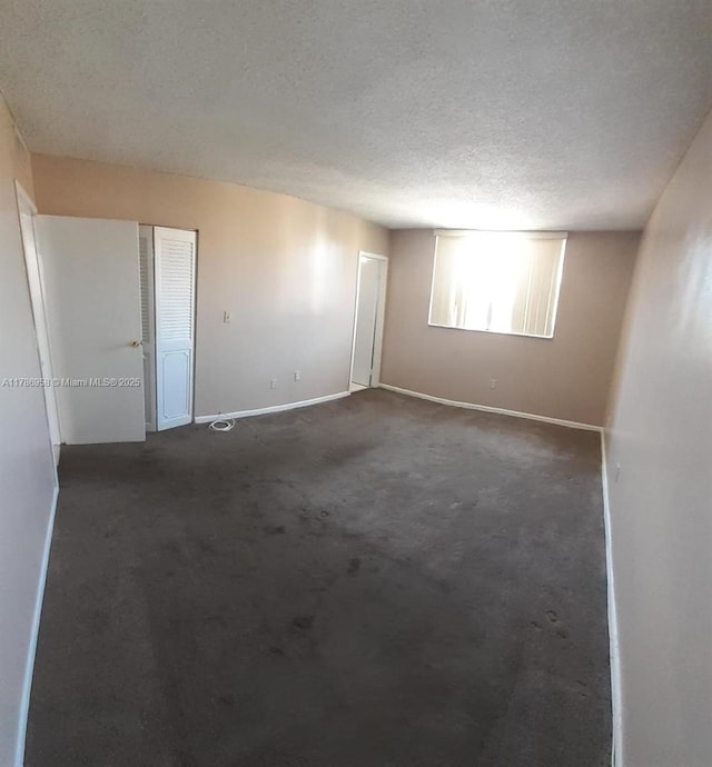 empty room with dark carpet, baseboards, and a textured ceiling