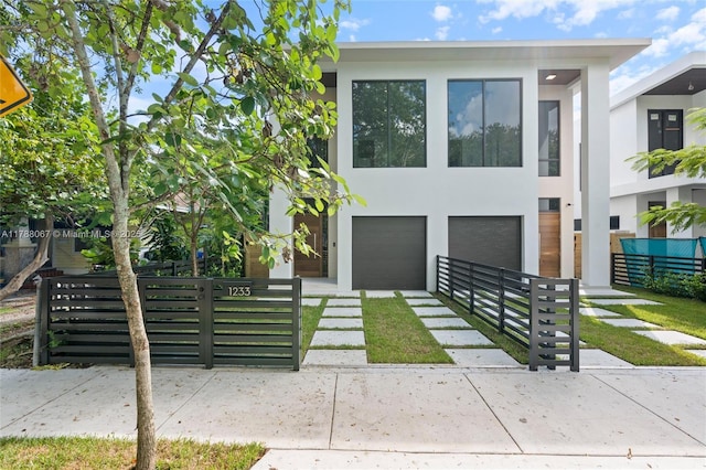 contemporary house featuring an attached garage, fence, stucco siding, and driveway