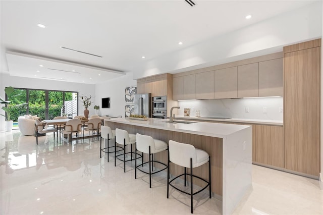 kitchen with a large island with sink, stainless steel appliances, a breakfast bar, a sink, and modern cabinets