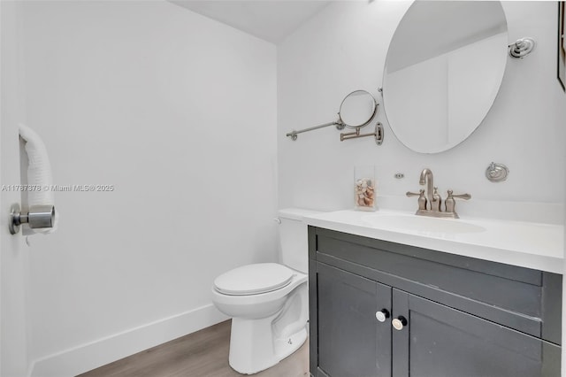 half bath featuring toilet, vanity, wood finished floors, and baseboards