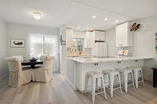 kitchen with white cabinets, a peninsula, light wood-style floors, and freestanding refrigerator