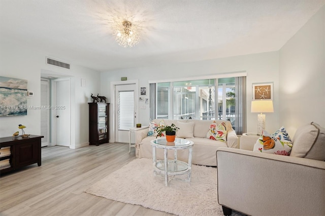 living room featuring a chandelier, light wood-style floors, visible vents, and baseboards
