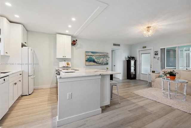 kitchen featuring visible vents, white appliances, a kitchen island, and light wood-style floors