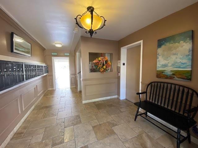 hall with stone tile floors, mail area, a wainscoted wall, and a decorative wall