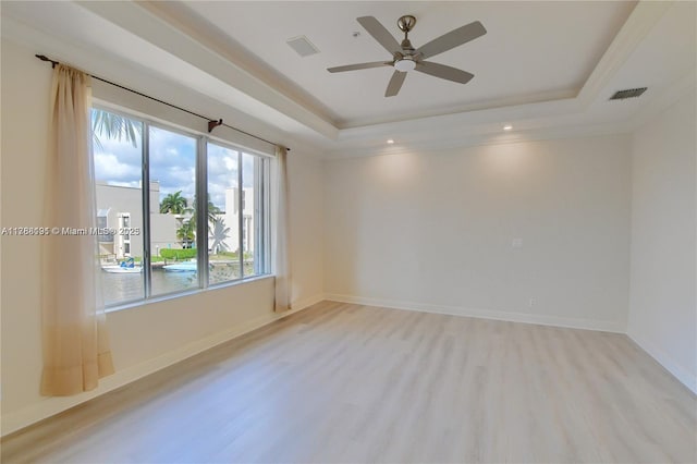 spare room with a ceiling fan, light wood finished floors, visible vents, and a raised ceiling