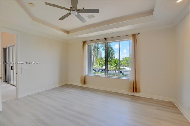 spare room featuring a raised ceiling, light wood-type flooring, visible vents, and ceiling fan