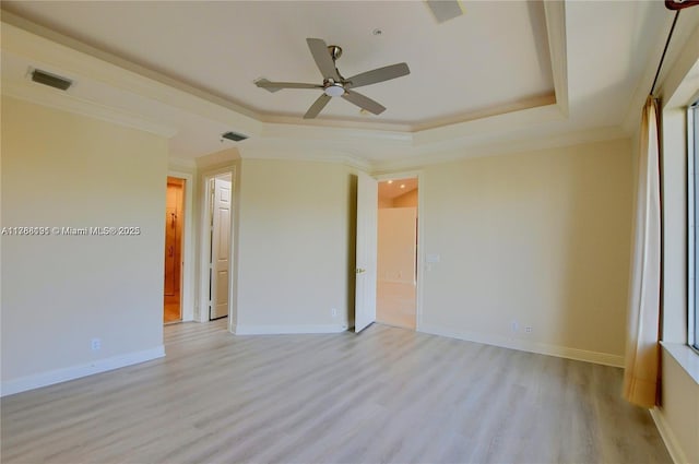 empty room with a tray ceiling, visible vents, a ceiling fan, light wood-style floors, and crown molding