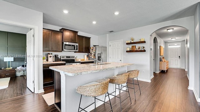 kitchen featuring dark brown cabinets, arched walkways, light countertops, dark wood finished floors, and appliances with stainless steel finishes