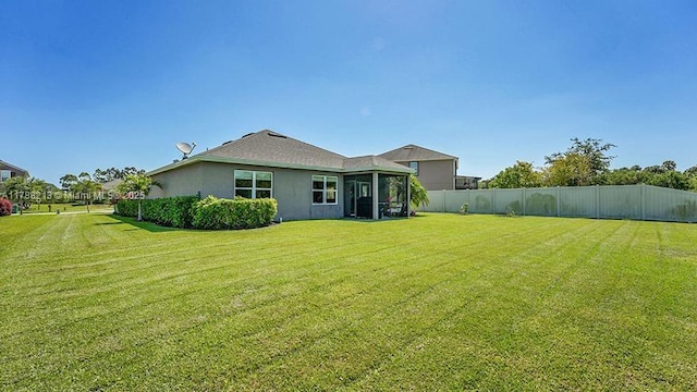 rear view of property with stucco siding, a yard, and fence
