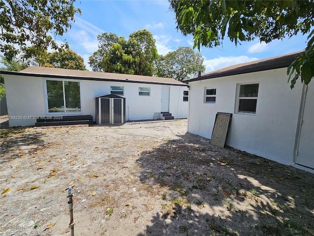 rear view of house featuring an outbuilding, a storage shed, entry steps, and stucco siding
