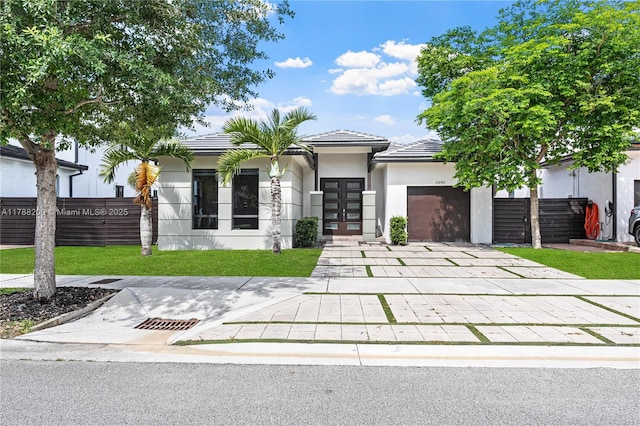 prairie-style house featuring concrete driveway, stucco siding, french doors, a front yard, and a garage