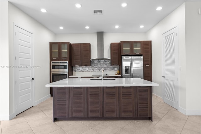 kitchen featuring a sink, stainless steel appliances, a center island with sink, wall chimney exhaust hood, and visible vents