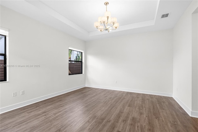 empty room featuring wood finished floors, a chandelier, a tray ceiling, baseboards, and visible vents
