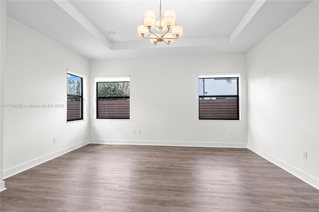 spare room featuring baseboards, wood finished floors, a tray ceiling, and a notable chandelier
