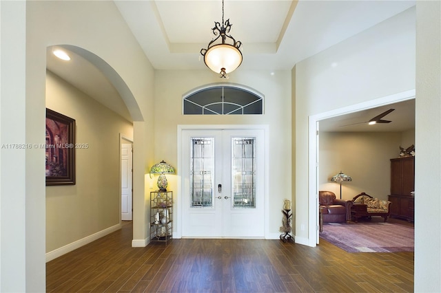 entrance foyer with french doors, arched walkways, dark wood-type flooring, and a raised ceiling
